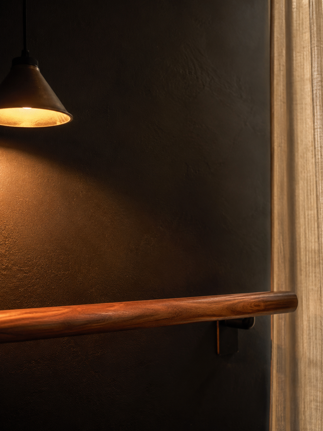 Détail de la barre walnut sous lampe pendante tungstène, texture du bois, mur noir mat